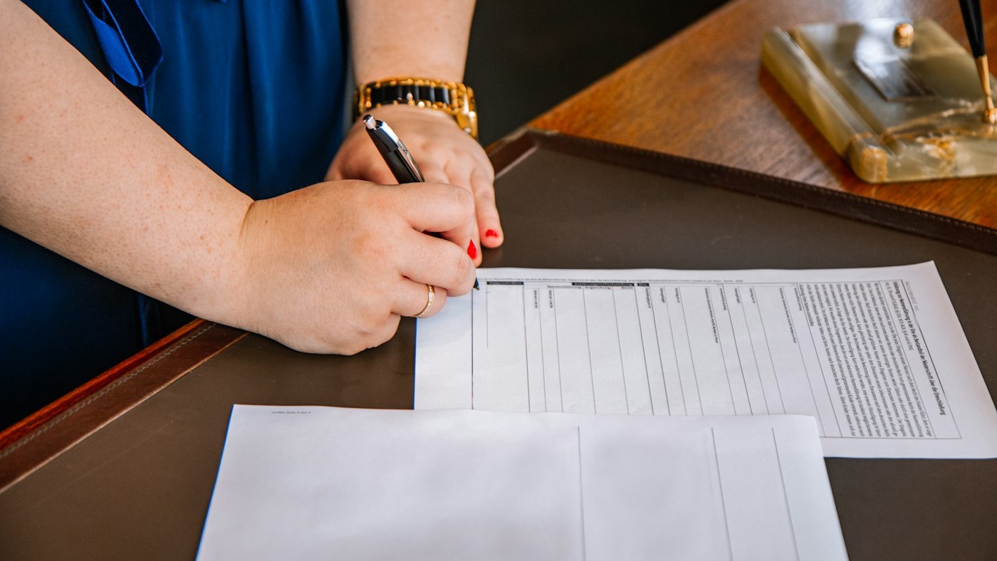A woman in a blue blazer signing a form at a desk